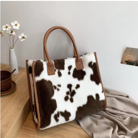 Warm Brown & Cream cow print faux fur tote bag on wooden table with flowers and magazine