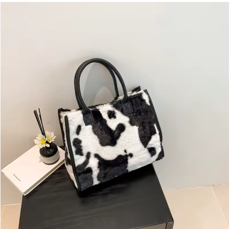 Classic Black & White cow print faux fur tote bag on black table with diffuser and notebook
